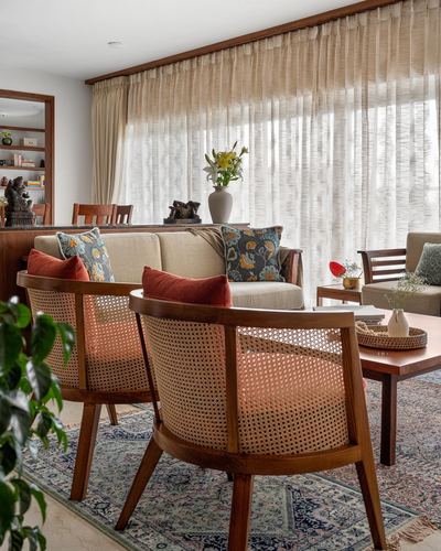 Cane-backed armchairs and sofa with printed cushions in a sunlit living room with sheer curtains