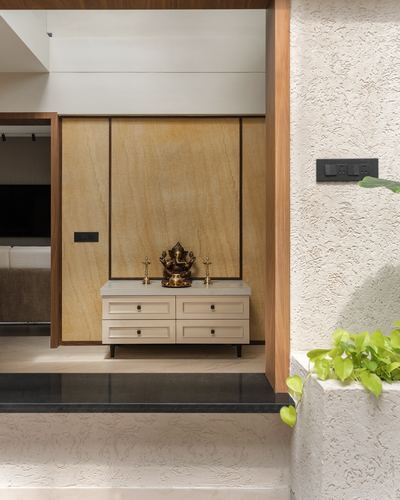 Pooja niche with brass Ganesha idol on white cabinet against warm stone-textured wall panel