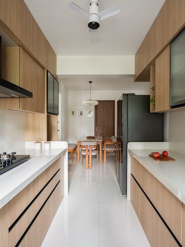 Wood-toned galley kitchen with white countertops opening onto a dining area with pendant light
