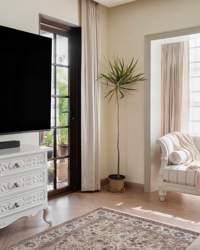 Living room corner with white carved dresser, tall plant, and glass door to balcony