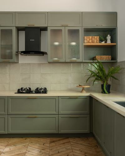 Sage green L-shaped kitchen with black chimney hood, tiled backsplash and chevron wood floor