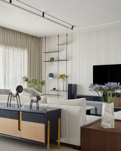 White living room with fluted wall paneling, hanging shelf, and dark wood sideboard with brass legs