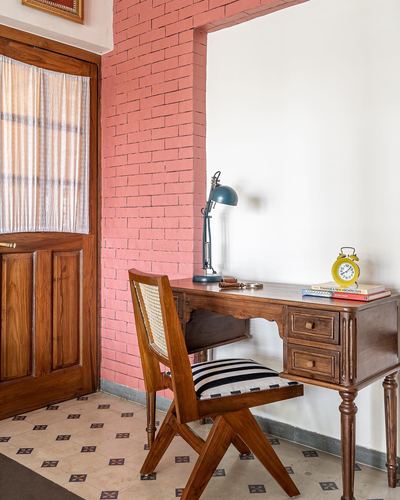 Wooden study desk with cane chair set against a pink brick alcove near a wooden door