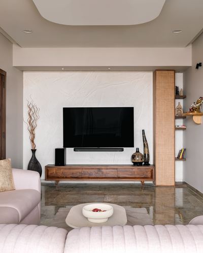 Living room with textured stone TV wall, wooden console, cane shelving niche, and marble floor