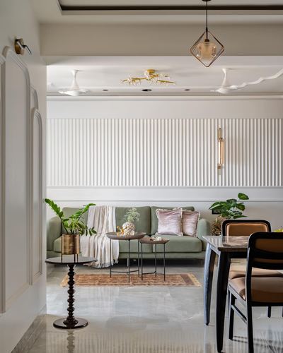 Living and dining area with green sofa, fluted white paneling, and marble floor in Ahmedabad apartment