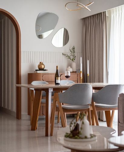 Dining area with wood table, grey upholstered chairs, and two organic mirrors above a fluted sideboard
