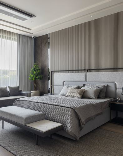 Grey upholstered bed against fluted grey wall with sheer curtains and marble-topped bench