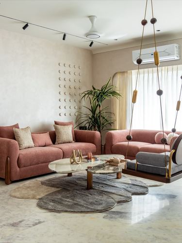 Living room with pink sofas, stone floor, cloud-shaped rugs, and a hanging wooden swing