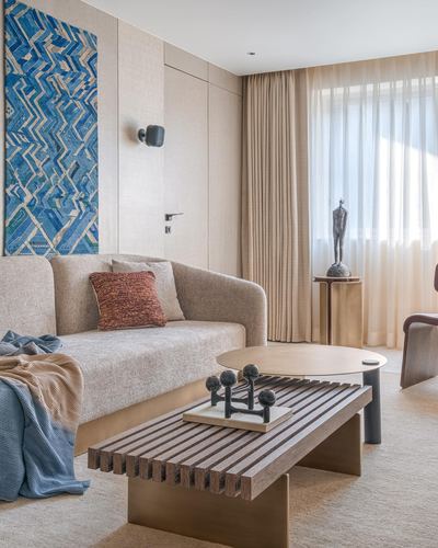 Beige living room corner with sofa, slatted wood coffee table, brass side table, and blue textile art