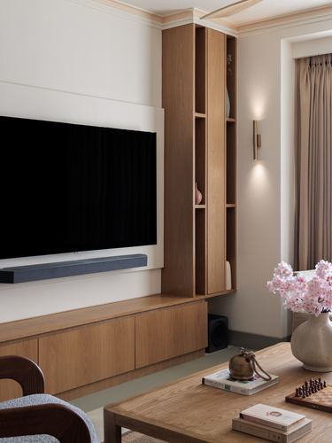Living room with wood tv console, shelving niche, brass sconce, and floral arrangement on coffee table