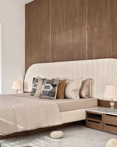 Bed with channel-tufted cream headboard against wood-panelled wall, wooden nightstand with lamp beside it