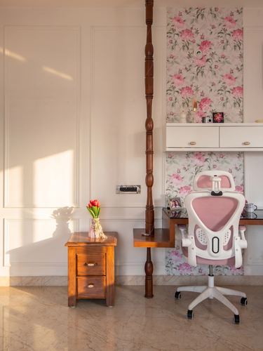 Study nook with floral wallpaper, white desk, pink ergonomic chair and wooden bedside table
