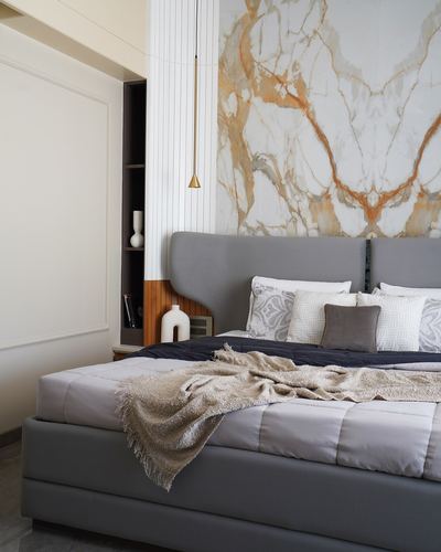Bedroom with grey upholstered bed against a veined orange-grey stone accent wall and brass pendant light.