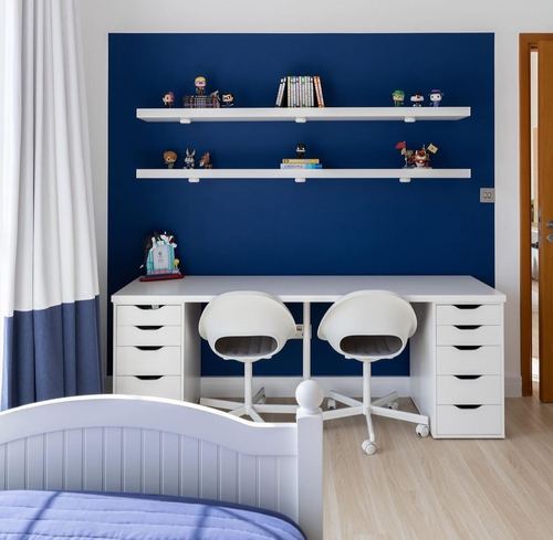 Kids bedroom with navy accent wall, floating shelves of figurines, and a white twin desk with two chairs