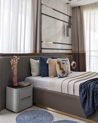 Bedroom with grey leather headboard, marble panel wall, brass pendant light and layered cushions