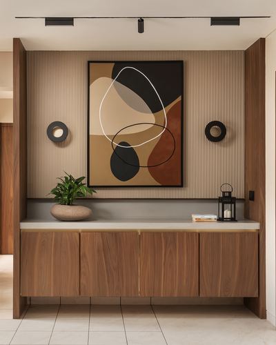 Wooden console with abstract art and round sconces in a foyer with fluted wall panels
