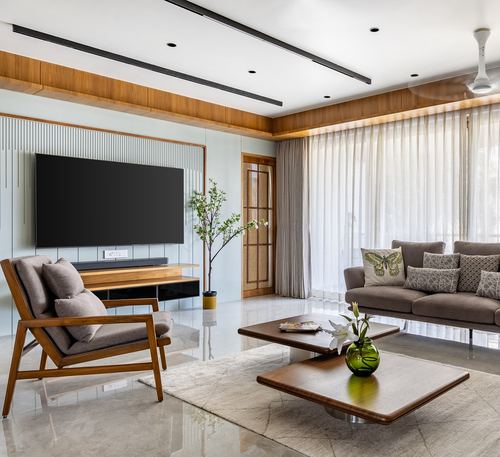 Living room with wood-panelled tv wall, cane door, sheer curtains, and layered wooden coffee tables on a rug