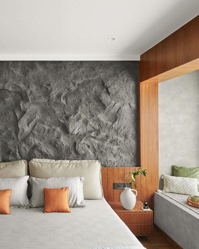 Bedroom with textured grey stone wall art, wood-framed window seat, and orange accent cushions