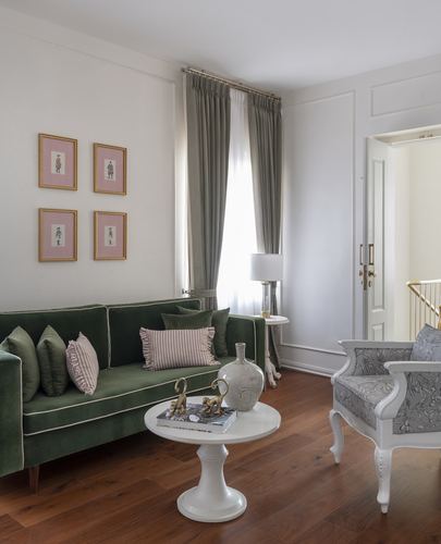Living room with green velvet sofa, floral armchair, and pink framed prints on wall