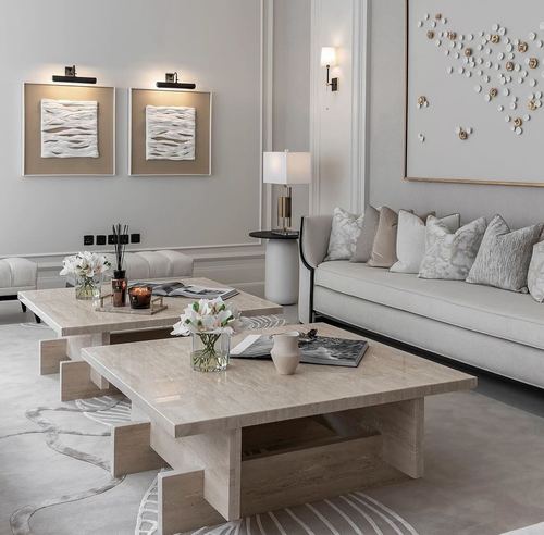 Neutral living room with travertine coffee tables, beige sofa, and textured wall art under sconce lighting