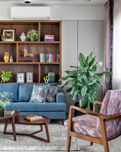 Living room with fluted wood bookshelf, blue sofa, and mauve armchair around a round coffee table