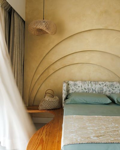 Bed with floral tufted headboard against arched plaster wall, rattan pendant light beside sheer curtain