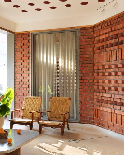 Curved perforated brick wall corner with two cane chairs and marble table in sunlit Jaipur homestay