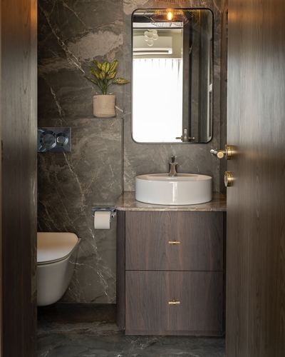 Dark stone bathroom with wood vanity, round vessel sink, wall-mounted toilet and mirror reflecting light fixture.