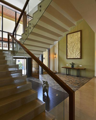 Floating stone staircase with glass railing beside an olive wall with carved panel and console table