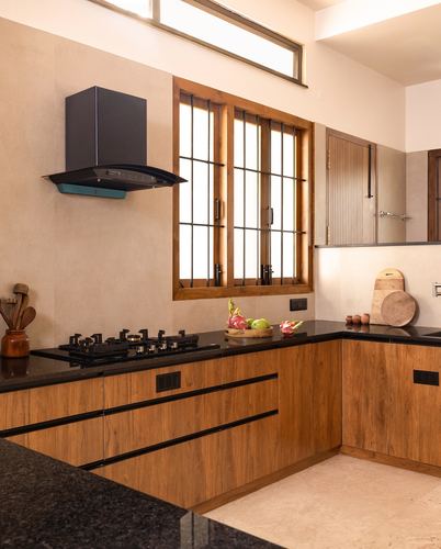 L-shaped wooden kitchen with black countertop, gas hob, and tall wooden window grille