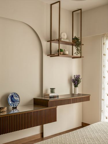 Fluted wood credenza with glass top below a hanging brass shelf against an arched cream wall
