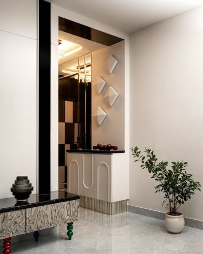 Foyer with fluted console, mirrored panel, geometric wall sconces and marble floor beside a potted plant