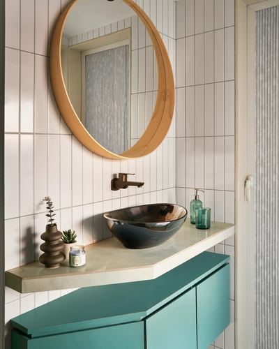 Round wood-framed mirror above teal vanity with dark vessel sink and stone counter