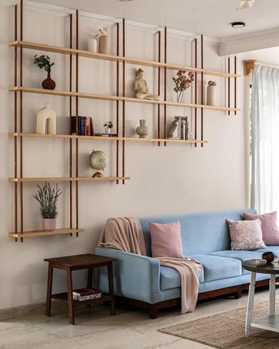 Living room with open wooden shelving styled with decor above a blue sofa with pink pillows