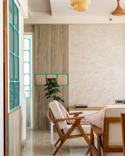 Living room corner with fluted wood paneling, turquoise-framed glass door, and teak armchair