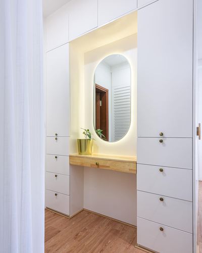 White wardrobe wall with backlit oval mirror and wooden console shelf holding a brass planter