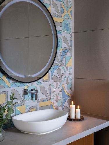 White vessel sink under round mirror beside colorful patterned tile strip and lit candles