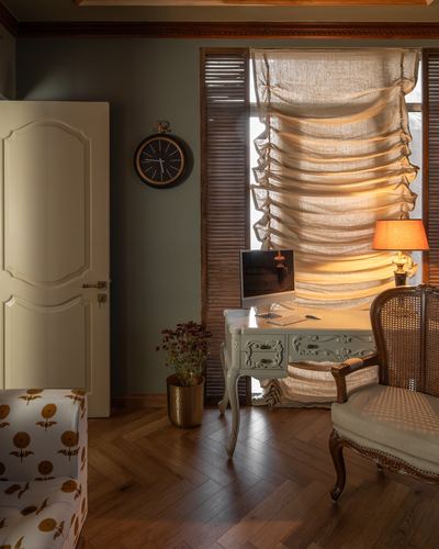 French-style study corner with carved desk, cane armchair, and ruched linen blind lit warmly