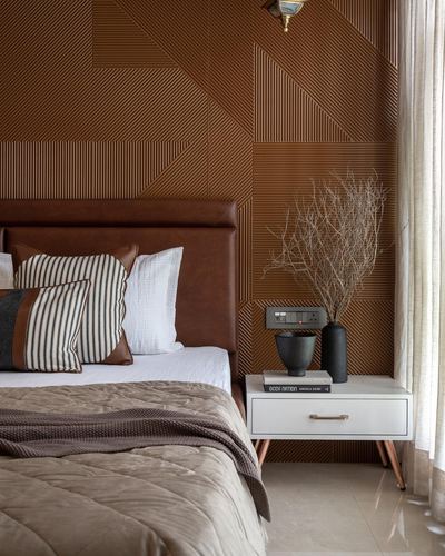 Bedroom corner with leather headboard against fluted wood-panel wall and white bedside table with dried branches