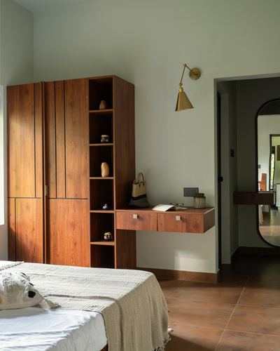 Wooden wardrobe and open shelving beside a floating console in a warm-toned bedroom with terracotta flooring