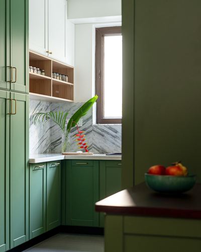 Green kitchen cabinetry with marble-look chevron backsplash and window, foreground dark countertop with fruit bowl