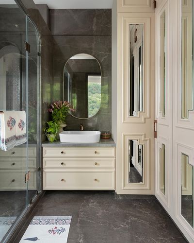 Bathroom vanity with oval mirror, vessel sink, dark marble walls and cream mirrored wardrobe