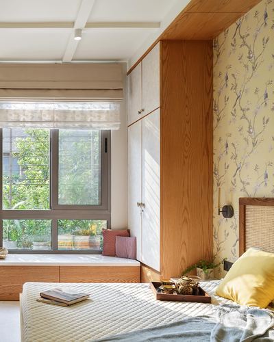 Sunlit bedroom with wooden wardrobe, window seat, cane headboard and floral wallpaper