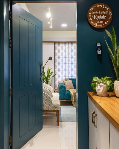 Open teal entry door revealing a living room with teal sofa, patterned blind and wooden nameplate on wall