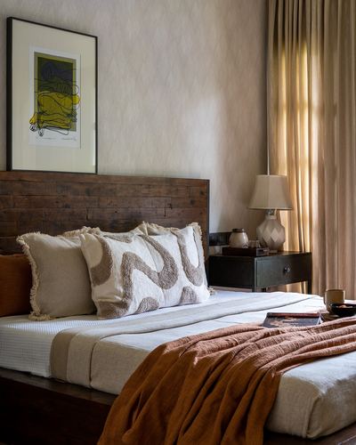 Bedroom with wood-plank headboard, textured pillows, rust throw, and curtained window with lamp.