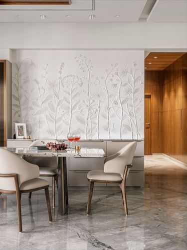 Dining table with cream chairs beneath a sculpted floral relief wall, marble floor leading to a wood-paneled hallway