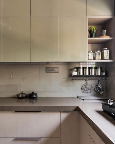 Corner of a modern kitchen with glossy green cabinets, open shelves, and steel utensil rack
