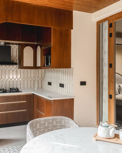 Wood-toned kitchen corner with arched cabinet fronts, patterned tile backsplash and marble dining table in foreground