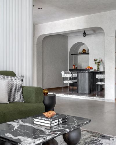 Living room with green boucle sofa, marble coffee table, and arched bar nook beyond textured walls