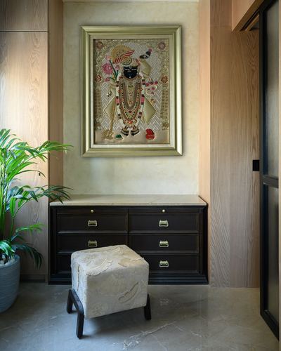 Entryway with framed devotional artwork above a dark wood console, marble top, and embroidered stool